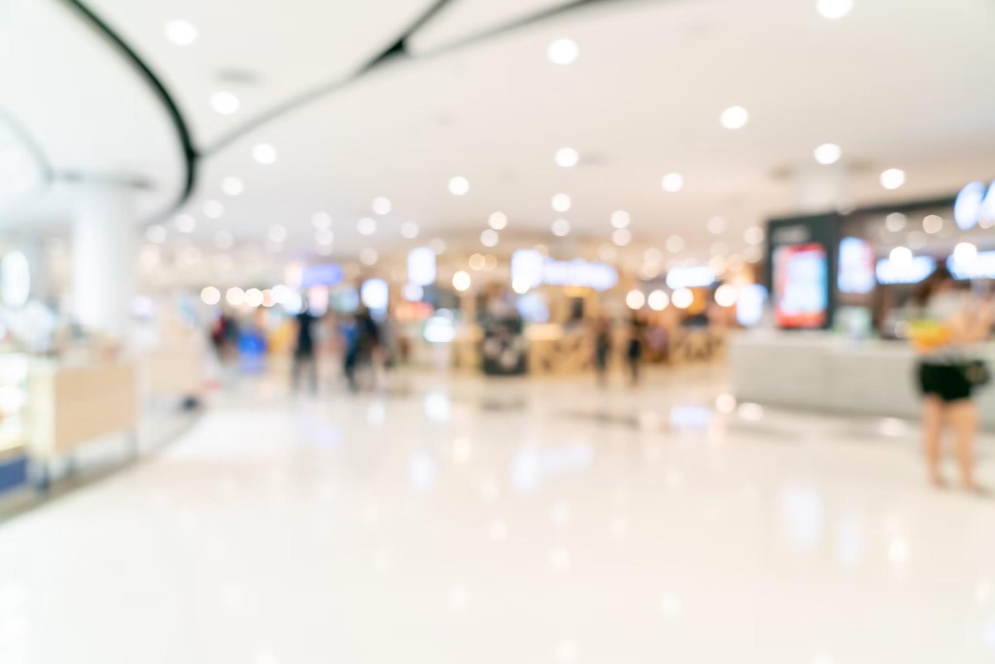 blurred out image of brightly lit shopping mall with shoppers in the background of the retail setting