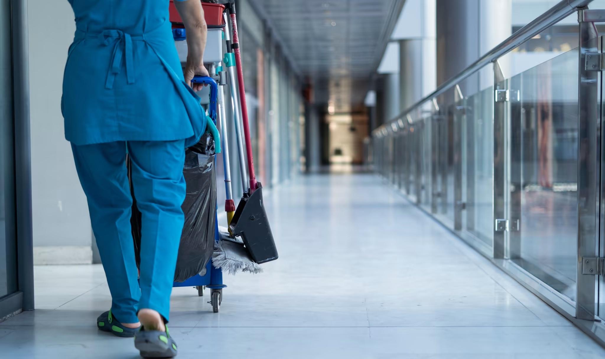 cleaning staff pushing cleaning cart through long hallway of large office building