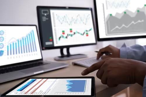 person analyzing data on computer screens and tablet in office 