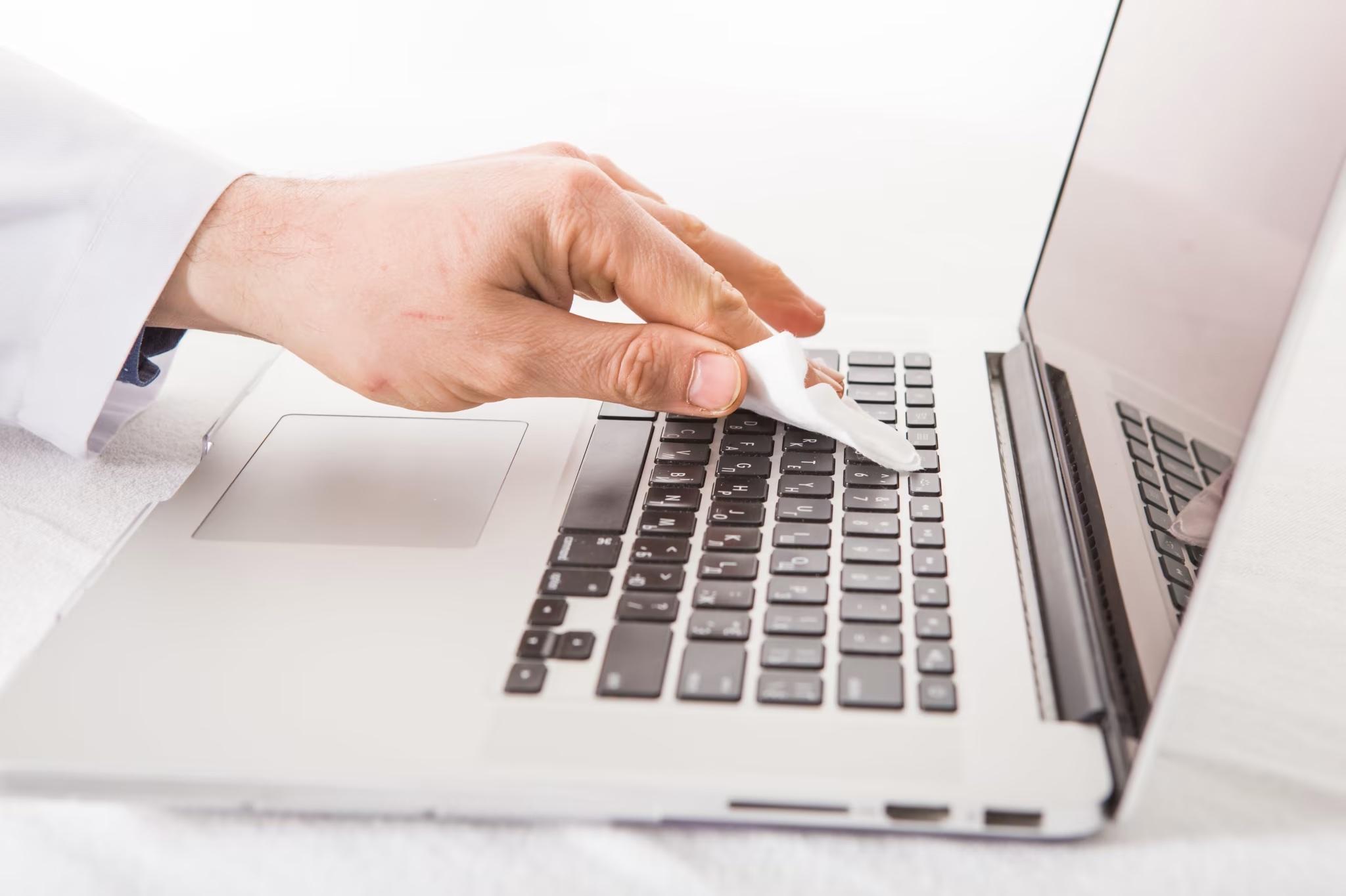 person wiping down a computer keyboard to help stop the spread of germs