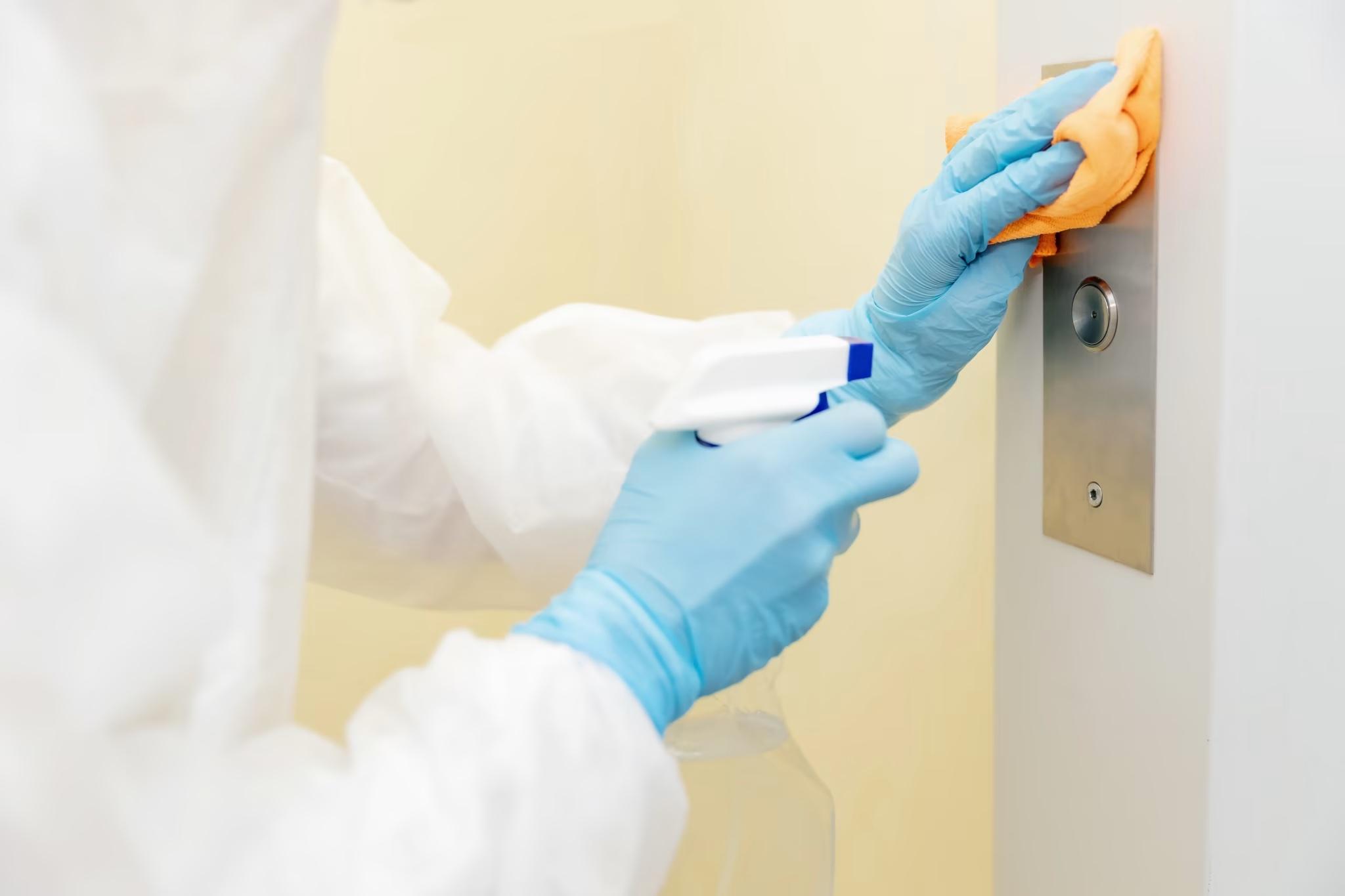 EVS staff cleaning elevator button in healthcare facility using disinfecting cloth