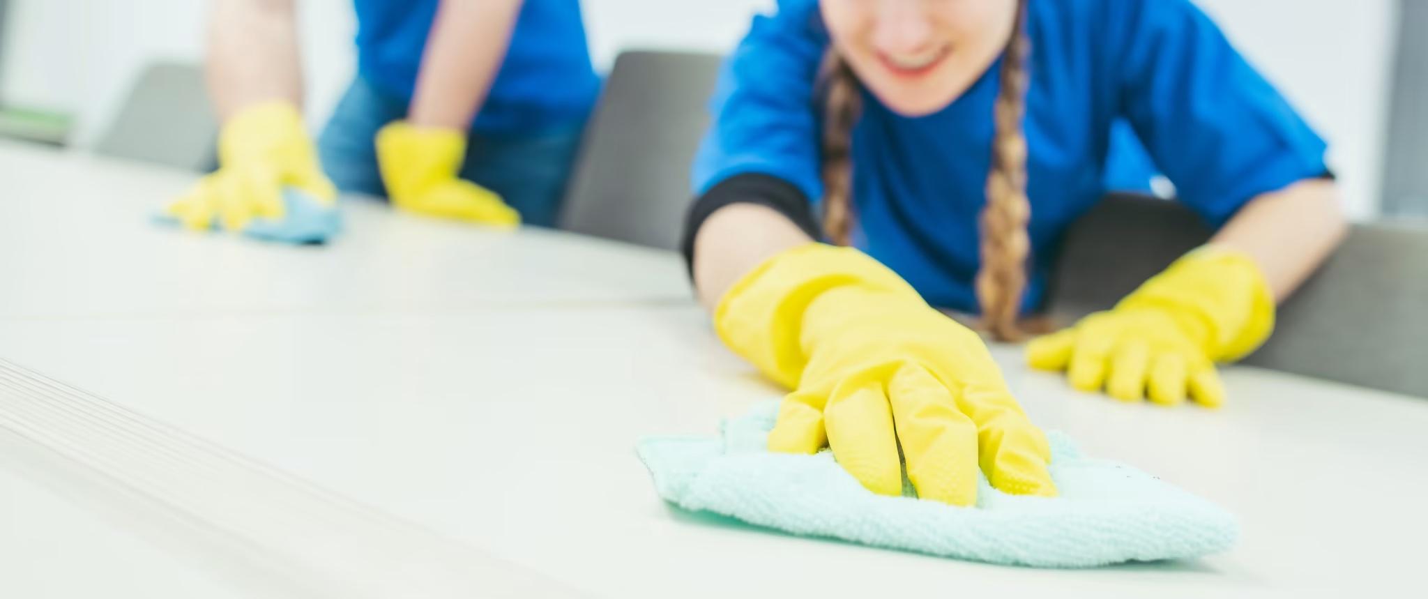 cleaning team member wearing yellow gloves cleaning office table