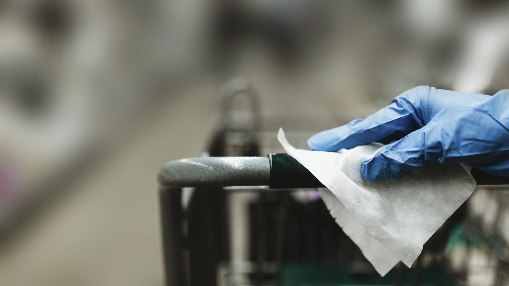 grocery store cart being wiped and sanitized by staff member wearing rubber gloves