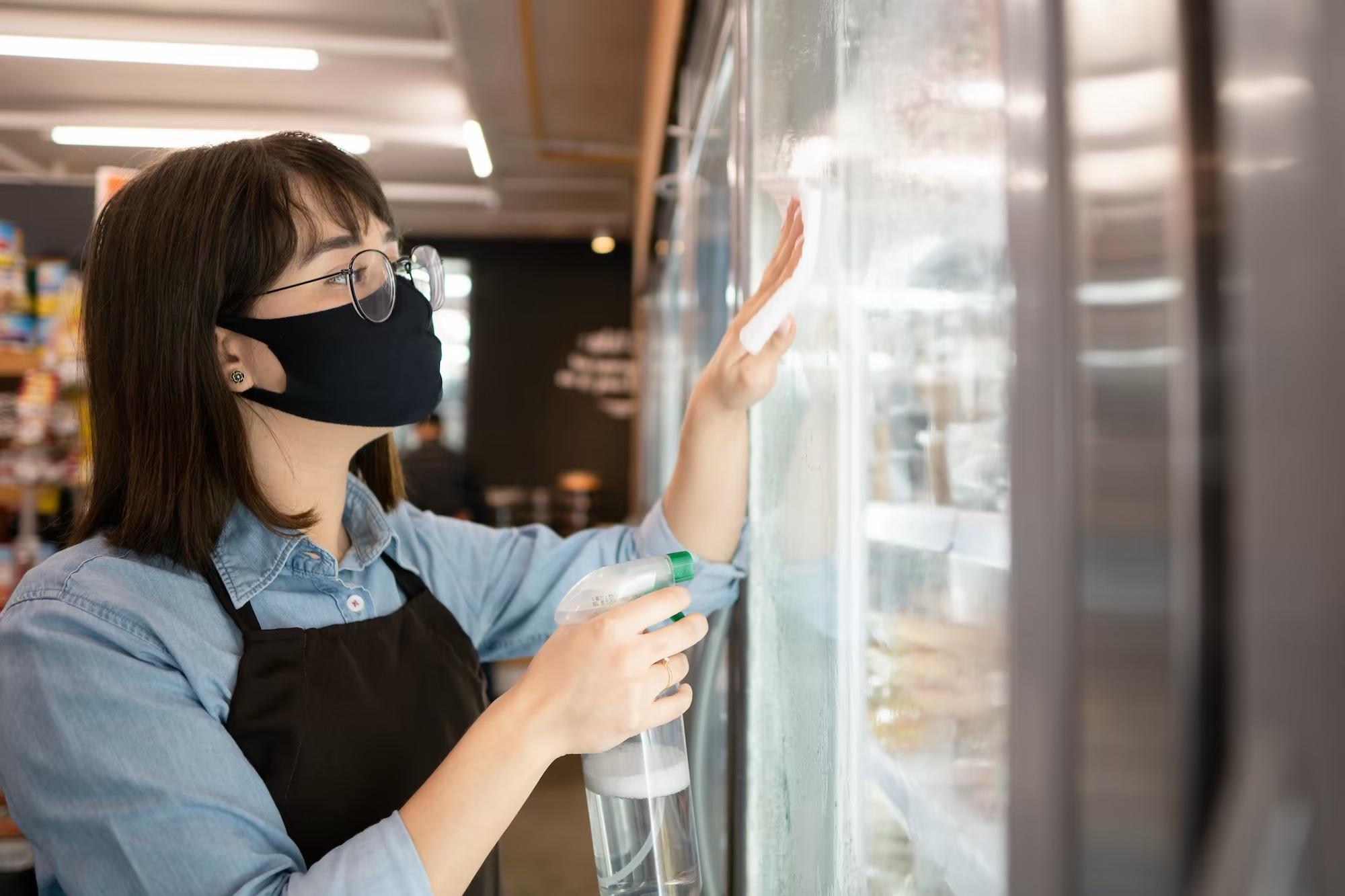 grocery store retail employee cleaning cooler doors with glass cleaner to keep things clean and shiny