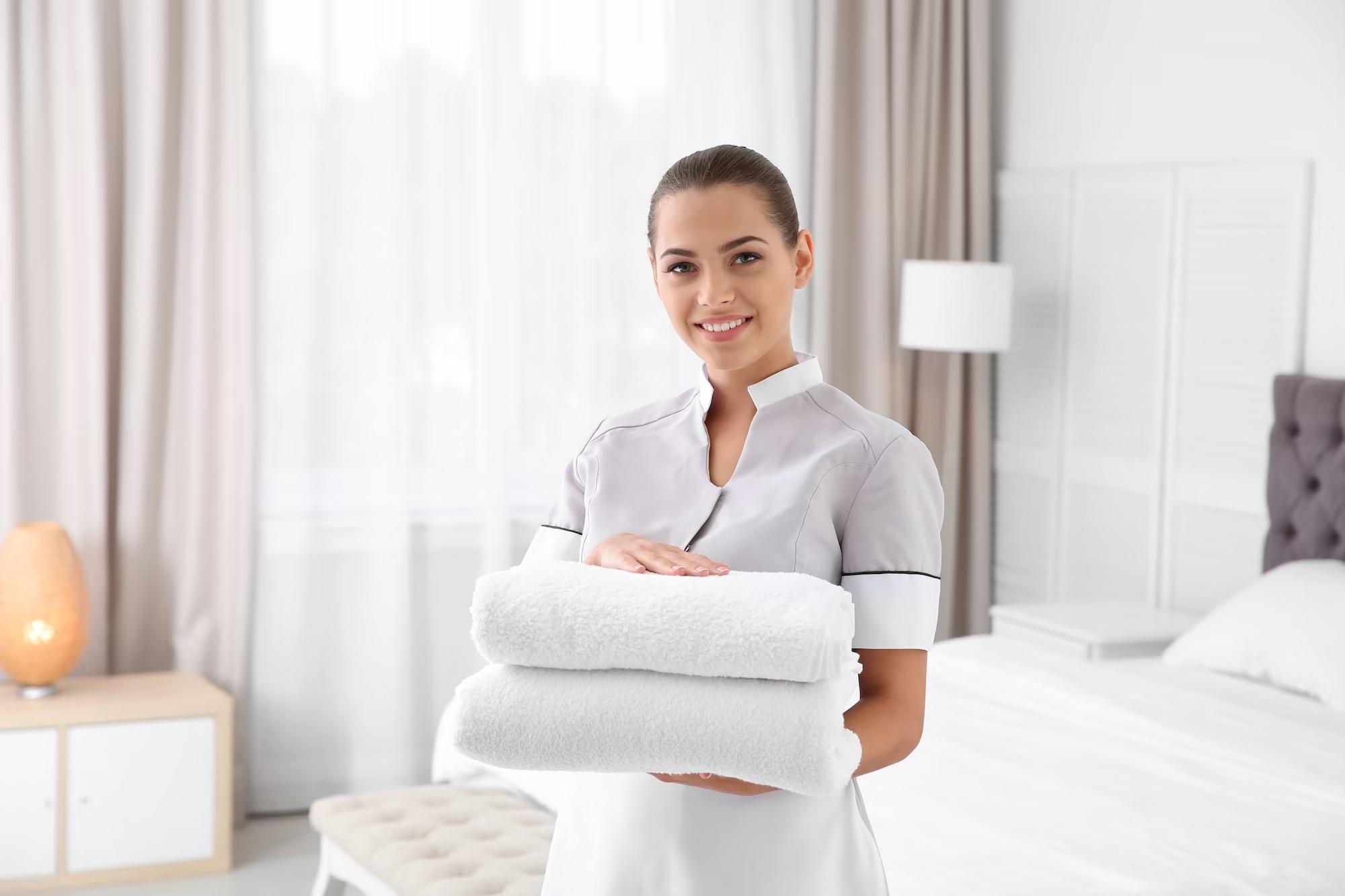 hotel housekeeping staff in hotel room holding neatly folded towels and looking happy