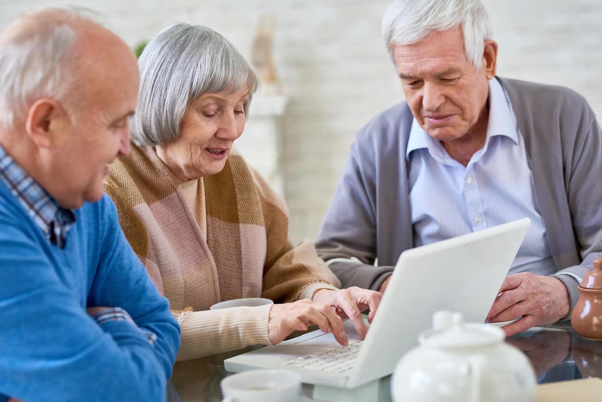 three seniors working together while using computer technology in a senior living facility